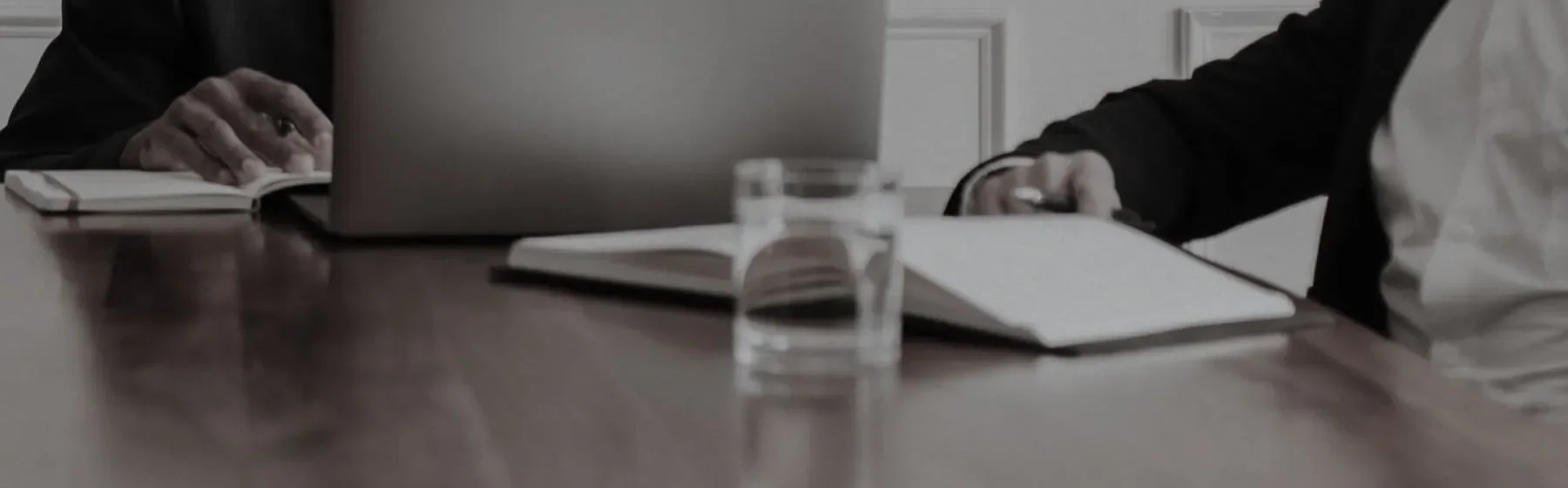 Two people either side of a table, an open notebook and a glass of water between them.