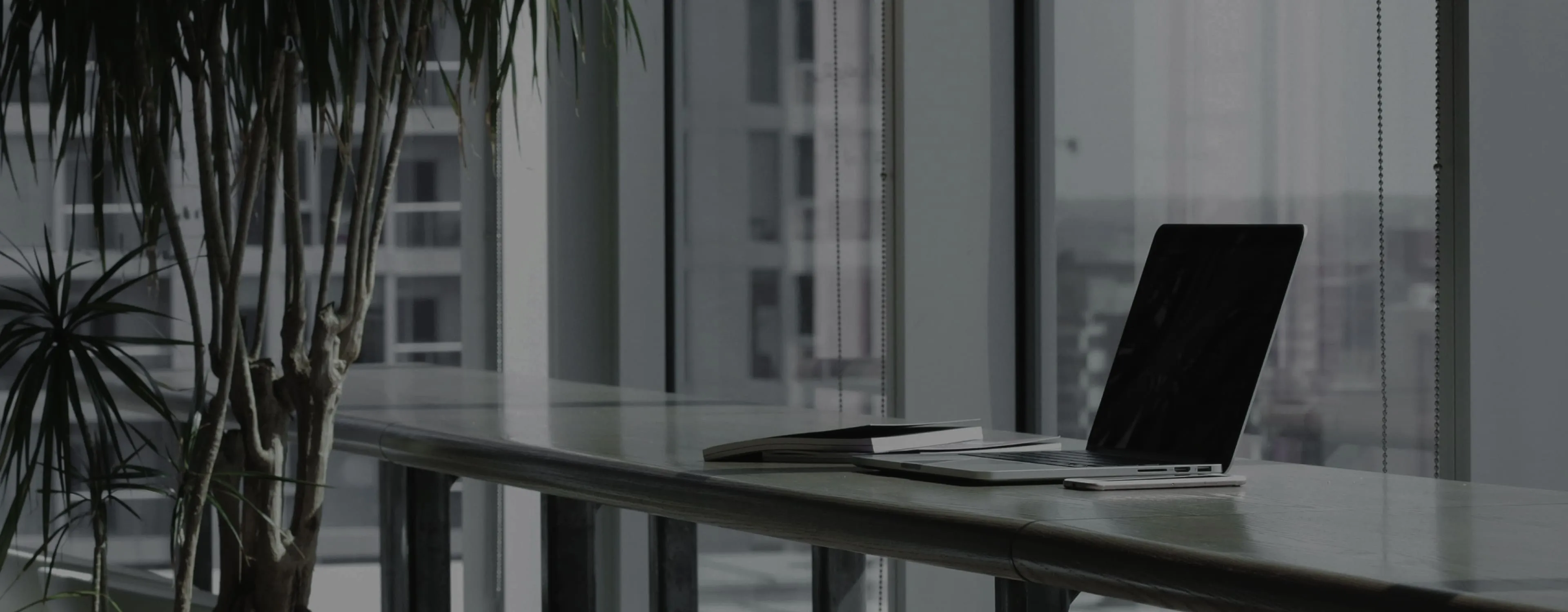 A desk beside a window, with a laptop and an open notebook.
